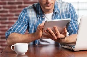 Advantages of free Wi-Fi. Close-up of young man working on digital tablet while sitting at his working place photo