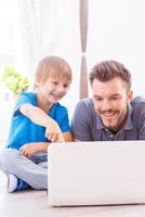 Spending time together. Happy father and son surfing the net at home while little boy pointing laptop monitor and smiling photo