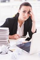 Failed again. Frustrated young woman in formalwear looking at camera while sitting at her working place photo