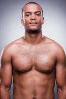 Strong and confident. Young shirtless African man looking at camera while standing against grey background photo