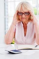 Financial troubles. Frustrated senior woman holding head in hands and looking at the bills laying on the table photo