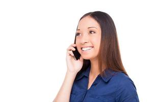 buena plática. bella joven asiática hablando por teléfono móvil y sonriendo mientras está aislada en blanco foto