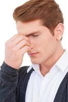 Feeling exhausted. Frustrated young man touching massaging his nose and keeping eyes closed while standing isolated on white photo