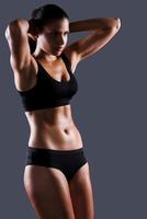 Proud of her perfect body. Beautiful young sporty woman with perfect body posing against grey background photo