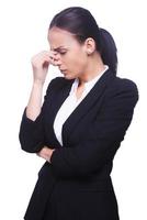 Depressed and hopeless. Side view of frustrated young woman in formalwear touching her nose and keeping eyes closed while standing isolated on white background photo