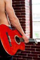 Guitar head. Close-up rear view image of shirtless man holding acoustic guitar while standing in front of the window photo
