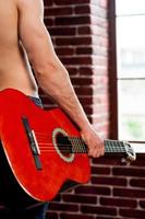 cabeza de guitarra imagen de vista trasera de primer plano de un hombre sin camisa sosteniendo una guitarra acústica mientras está de pie frente a la ventana foto