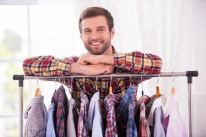 camisas todos los días. hombre joven guapo apoyado en el armario con diferentes camisas y sonriendo foto