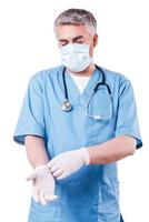 Surgeon wearing gloves. Confident surgeon in surgical mask wearing gloves while standing isolated on white photo
