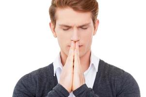 Praying for business. Concentrated young man holding hands clasped near mouth and keeping eyes closed while standing isolated on white photo