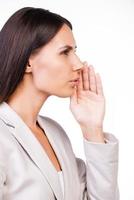 Telling fresh gossips. Side view of beautiful young businesswoman in suit telling gossips while standing against white background photo