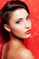 Beauty with stylish hairstyle. Rear view of beautiful young shirtless woman standing against red background and looking at camera photo