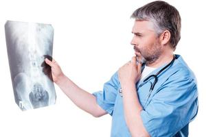médico examinando la imagen de rayos x. un médico de pelo gris maduro y pensativo que examina la imagen de rayos X mientras está de pie aislado en blanco foto