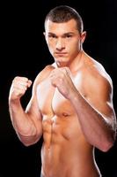 Ready to fight. Portrait of serious young shirtless man looking at camera while standing against black background photo