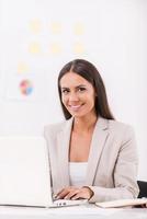 Businesswoman at work. Beautiful young businesswoman using computer and smiling while sitting at her working place photo