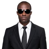 Elegant and cool. Serious young African man in formalwear and sunglasses looking at camera while standing isolated on white background photo