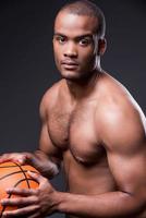 I love basketball. Young shirtless African man holding basketball ball and looking at camera while standing against grey background photo