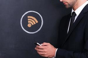 Internet connection. Close-up of young man holding telephone while standing against sharing  symbol chalk drawing on blackboard photo