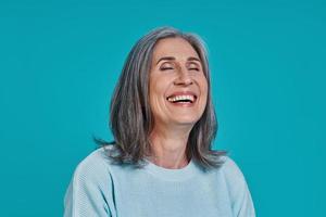 Headshot of mature beautiful woman laughing while standing against blue background photo