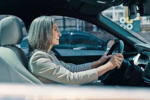 Side view of mature beautiful woman in smart casual wear smiling while driving car photo