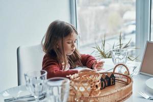 linda niña pintando algo mientras se sienta en la cocina en casa foto