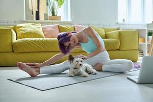 Beautiful young woman in sports clothing doing stretching exercises with her dog at home photo