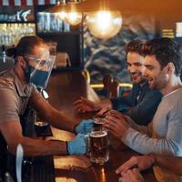 jóvenes sonrientes con ropa informal bebiendo cerveza y uniéndose mientras están sentados en el pub foto