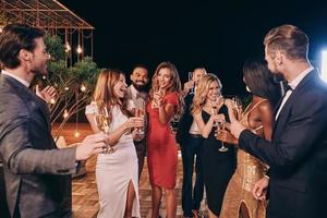grupo de personas hermosas en ropa formal comunicándose y sonriendo mientras pasan tiempo en una fiesta de lujo foto
