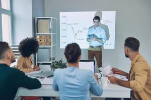 Group of young modern people in smart casual wear analyzing data on projection screen in the office photo