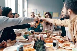 grupo de jóvenes con ropa informal recogiendo pizza y sonriendo mientras cenan en el interior foto