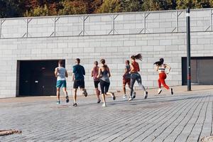 toda la longitud de los jóvenes en ropa deportiva trotando mientras hacen ejercicio al aire libre foto