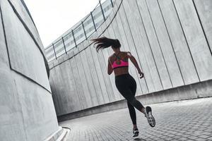 logrando mejores resultados. vista trasera completa de una mujer joven con ropa deportiva trotando mientras hace ejercicio al aire libre foto