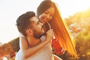 Handsome young man carrying his girlfriend on shoulders and enjoying drink photo