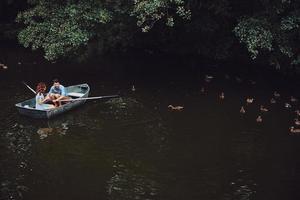 Beauty of nature. Top view of beautiful young couple feeding ducks while rowing a boat photo