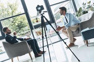 Creating interesting content. Two young men in smart casual wear talking while making new video indoors photo