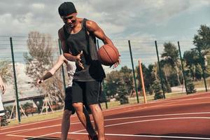 feliz de jugar dos jóvenes vestidos con ropa deportiva jugando baloncesto mientras pasan tiempo al aire libre foto