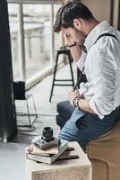 Frustrated photographer. Frustrated young man in white shirt and suspenders looking away while leaning on sofa photo