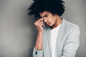 Feeling tired. Frustrated young handsome African man looking exhausted while standing against grey background photo