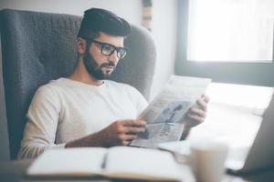 leyendo un periódico fresco. joven seguro de sí mismo con anteojos leyendo el periódico mientras está sentado en la oficina o en la cafetería foto