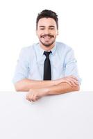 Confident business expert. Handsome young man in shirt and tie leaning at the copy space and keeping arms crossed while standing against white background photo