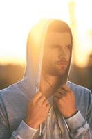 Confident in his forces. Serious young man adjusting his hood and looking away while standing outdoors photo