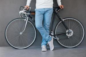 Man with bicycle. Close-up of man leaning at his bicycle while standing against grey background photo