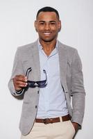 Expressing his good mood. Confident young African man carrying his sunglasses and smiling while standing against white background photo