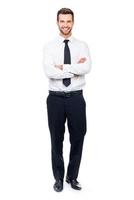 Confident businessman. Full length of smiling young businessman keeping arms crossed and looking at camera while standing against white background photo