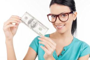 Rich and beautiful. Cheerful young woman in glasses holding one hundred dollar bill in her hands and smiling while standing isolated on white photo