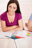 Smart beauty. Top view of beautiful female student sitting at the desk and smiling at camera photo