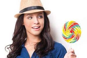 Extremely big lollipop. Young beautiful woman in funky looking at big lollipop and keeping mouth open while standing against white background photo