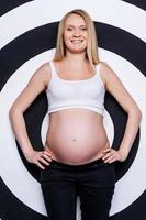 Beautiful pregnant woman. Beautiful pregnant woman holding hands on hip while standing against target background photo