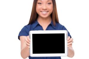 Copy space on her tablet. Beautiful young Asian woman showing her digital tablet and smiling while standing isolated on white photo