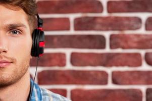 Music is my life. Handsome young man in headphones looking at camera while standing against brick wall photo